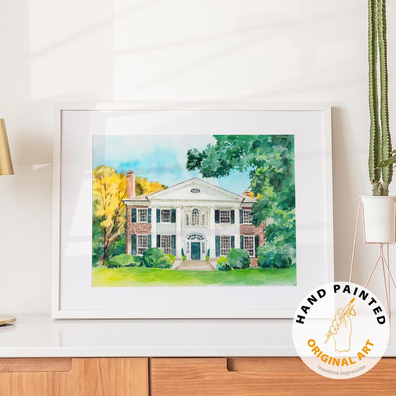May include: Watercolor painting of a stately white house with black shutters, a green lawn, and surrounding trees. The artwork is framed in a white border and features a "Hand Painted Original Art" sticker.