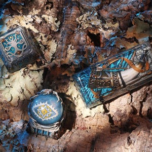 May include: Three artisan keycaps featuring intricate designs: a square keycap with a silver tree motif, a spherical keycap with a central eye graphic, and a rectangular keycap displaying a detailed horn and arrow illustration in blue and silver.