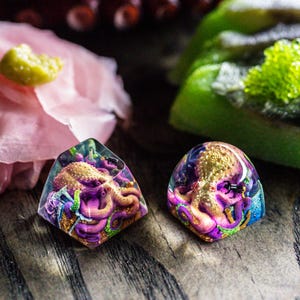 May include: Two resin keycaps featuring a purple octopus with gold accents. The keycaps are translucent and have a detailed design.
