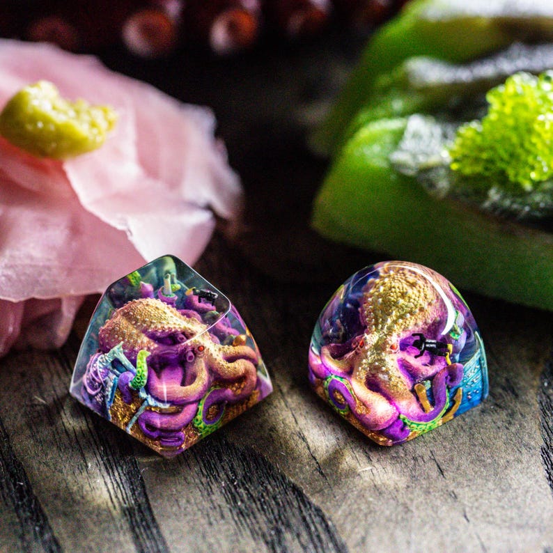 May include: Two resin keycaps featuring a purple octopus with gold accents. The keycaps are translucent and have a detailed design.