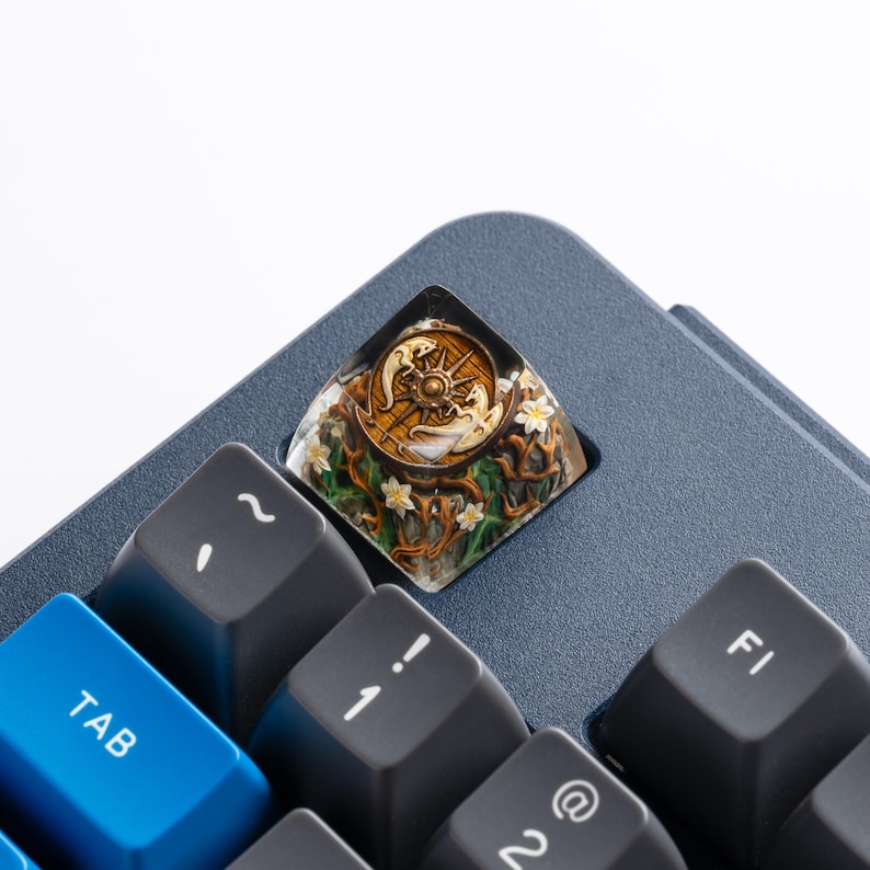 May include: A custom artisan keycap featuring a clear resin top with an embedded miniature scene. The design includes a circular wooden-style compass emblem, two white dragon figures, and a base of brown twisted branches with small white flowers.
