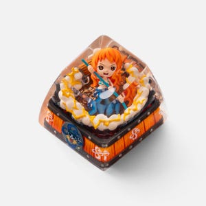 May include: A custom artisan keycap featuring a character with orange hair and a blue outfit. The keycap is encased in a clear resin, with a detailed design of a character from the One Piece anime series. The keycap has a black and orange base.