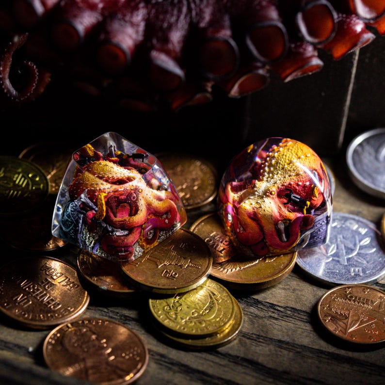May include: Two clear dice with an octopus design inside. The dice are red, orange, and yellow with a purple and blue background. The dice are sitting on a pile of copper and gold coins.
