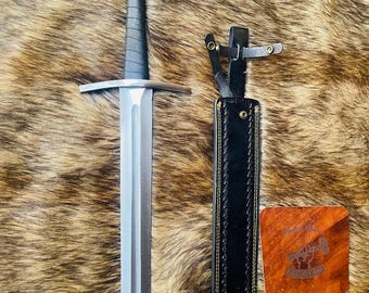 May include: A silver sword with a black leather handle and scabbard. The scabbard has a brown leather strap with brass rivets. The sword is on a brown fur background.