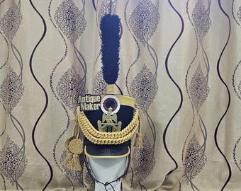May include: A navy blue and gold military hat with a tall, dark blue plume. The hat features gold trim, a gold chain, and a badge. The text "Antique Maker" is visible on the hat.