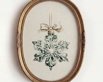 Könnte beinhalten: Eine Aquarellillustration eines dunkelgrünen, schneeflockenförmigen Weihnachtsschmucks, der an einer dünnen Schnur mit einer hellbeigen Schleife hängt und in einem verzierten, ovalen Goldrahmen mit geprägten Details präsentiert wird.