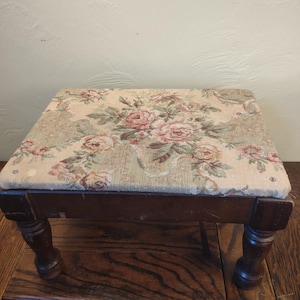 May include: A wooden footstool with turned legs and a floral patterned fabric top.