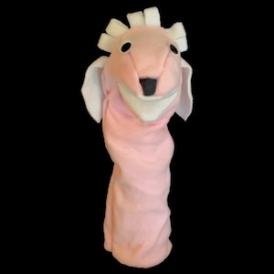 May include: A pink plush puppet in the shape of a sheep, with white ears and a white fringe on its head. The puppet has a black nose and eyes, and a white mouth. The puppet is designed to fit over a hand.