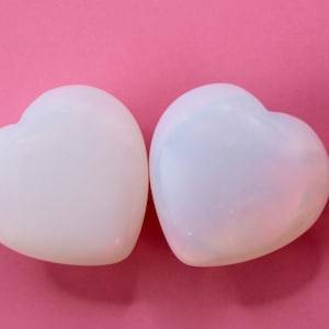 May include: Two white heart-shaped polished stones on a pink background.