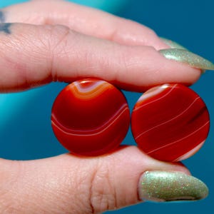 May include: Pair of red agate stone ear gauges with white swirling patterns.