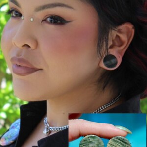 A bold pair of Green Jasper Double Flare Plugs sits elegantly on a neutral surface, radiating natural strength and earthy charm. Each plug is carved from genuine Green Jasper, showcasing deep olive and forest tones, marbled with organic patterns of b