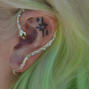 May include: A gold snake ear cuff with clear rhinestones. The cuff is worn on the upper part of the ear and wraps around the earlobe.