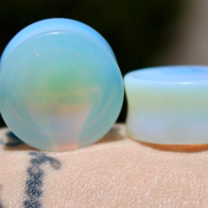 May include: Two iridescent opal ear gauges, one is a teardrop shape and the other is a cylinder shape.