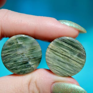 A bold pair of Green Jasper Double Flare Plugs sits elegantly on a neutral surface, radiating natural strength and earthy charm. Each plug is carved from genuine Green Jasper, showcasing deep olive and forest tones, marbled with organic patterns of b