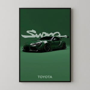 Peut inclure: Une affiche encadrée représentant une voiture de sport Toyota Supra vert foncé avec un aileron arrière, sur un fond vert uni. Le mot Supra est écrit dans une police blanche stylisée au-dessus de la voiture, et TOYOTA est inscrit en blanc en dessous.