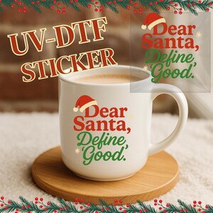 May include: A white ceramic mug with the text "Dear Santa, Define Good" in red and green, with a Santa hat graphic. The mug is on a wooden coaster, with a festive Christmas garland border.