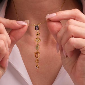 May include: A gold-tone chain necklace featuring a vertical drop pendant composed of six distinct, multi-colored gemstones in various shapes, including rectangular, oval, and heart-cut stones, set in gold-tone metal frames along the center.