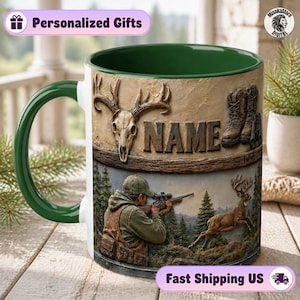 May include: A ceramic mug with a dark green interior and handle, featuring a hunting-themed graphic. The design includes a deer skull, a pair of boots, the word NAME, and an illustration of a person aiming a rifle at a leaping deer.