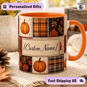 May include: A ceramic mug with an orange interior and handle, featuring a patchwork design of pumpkins, autumn leaves, and plaid patterns. A central rectangular label on the front displays the text Custom Name in a black cursive font.