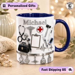 Puede incluir: Una taza de cerámica blanca con interior y asa azul oscuro, que presenta el nombre Michael y varias ilustraciones médicas como un estetoscopio, jeringa, portapapeles y maletín, con dijes metálicos colgantes en la base.