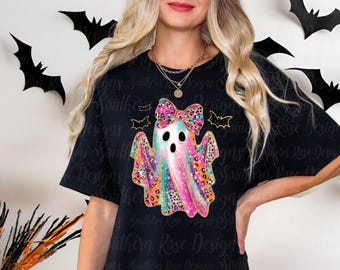 May include: Black t-shirt featuring a colorful ghost design with a bow and leopard print accents. The ghost has three eye holes and is surrounded by bats. The shirt is a Halloween-themed design.