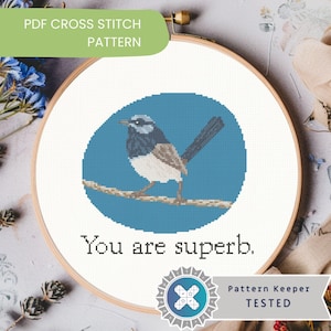 May include: A cross-stitch pattern in a wooden hoop features a blue bird on a branch against a blue background. The text "You are superb" is stitched below the bird. The top of the hoop has the text "PDF CROSS STITCH PATTERN".