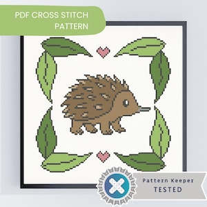 May include: Cross stitch pattern featuring a brown echidna with a long snout, surrounded by green leaves and pink hearts. The text "PDF CROSS STITCH PATTERN" is at the top, and "Pattern Keeper TESTED" is at the bottom. The design is framed in a black square.