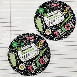 May include: Two black and white notebook paper-themed coasters with the word "TEACH" in colorful letters. Each coaster has a green cup, a pencil, a paperclip, a flower, and a composition notebook with the text "COMPOSITION" and a teacher's name.