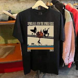 Puede incluir: Camiseta negra con un gr&aacute;fico de la pel&iacute;cula "Spider-Man: Into the Spider-Verse". El dise&ntilde;o incluye siluetas de personajes en un puente, con el texto "SPIDER-MAN: INTO THE SPIDER-VERSE" y "EST. 2018."