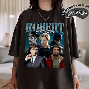 May include: Black t-shirt featuring a graphic print of Robert Pattinson in various roles. The text "ROBERT Pattinson" is printed in blue on the shirt.