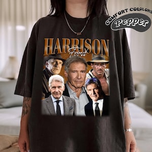 May include: Black t-shirt with a vintage-style graphic of Harrison Ford. The graphic features multiple images of Ford from different movies, including Indiana Jones and Star Wars. The text "Harrison Ford" is printed in brown letters above the images.