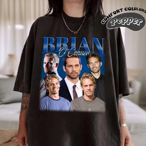 May include: Black t-shirt with a graphic print of four men. The text "BRIAN O'CONNER" is printed in blue letters above the image. The text "COMFORT COLORS Pepper" is printed in white letters on a red circle in the top right corner of the image.