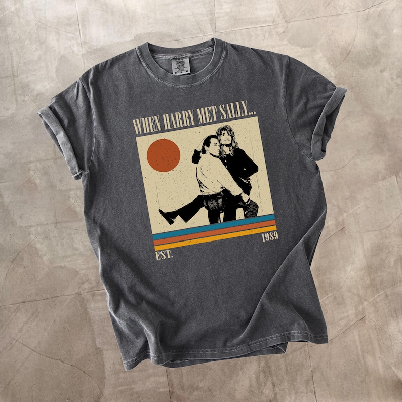 Puede incluir: Camiseta gris oscuro con un dise&ntilde;o gr&aacute;fico de la pel&iacute;cula "Cuando Harry encontr&oacute; a Sally...". El dise&ntilde;o incluye una imagen de los dos personajes principales, un sol y el a&ntilde;o 1989. La camiseta tiene las mangas dobladas.