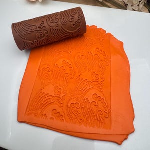 May include: A brown rolling pin with a cloud pattern design. The rolling pin is used to create an imprint on orange fondant.