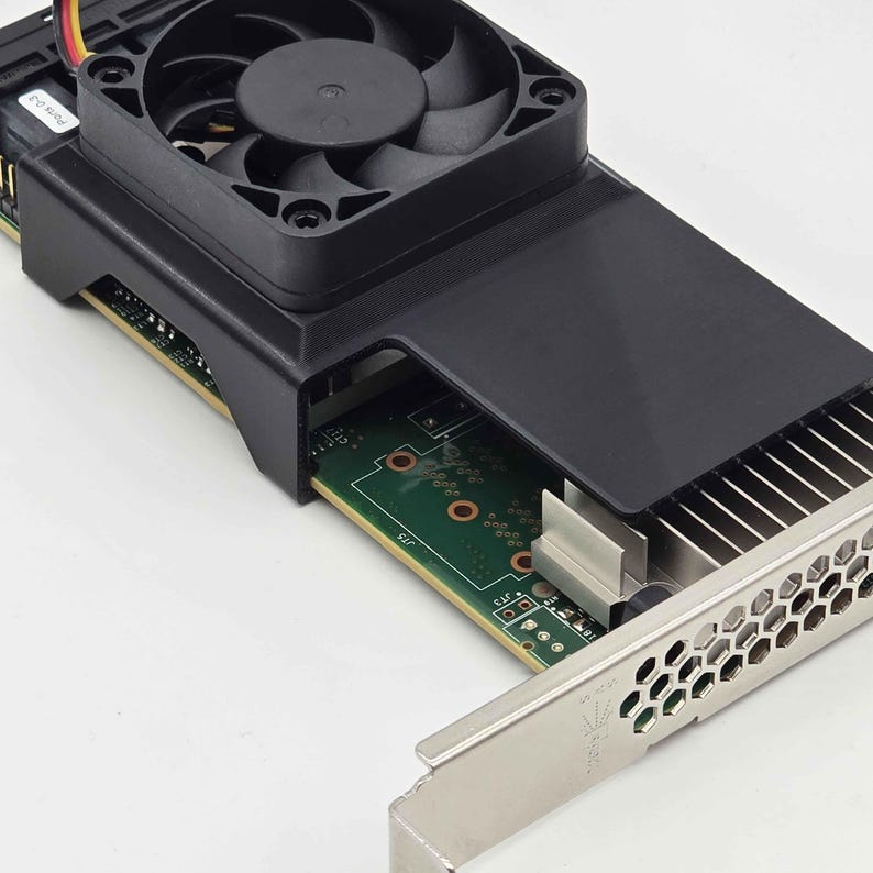 May include: A black and silver computer graphics card with a cooling fan. The card has a green circuit board with various components and a metal bracket with a honeycomb pattern. The fan is black and sits atop a black plastic housing.