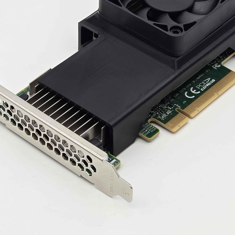 May include: A black computer component with a silver metal bracket and a black fan. The component has a series of metal fins and a green circuit board. The fan is located at the top of the component.