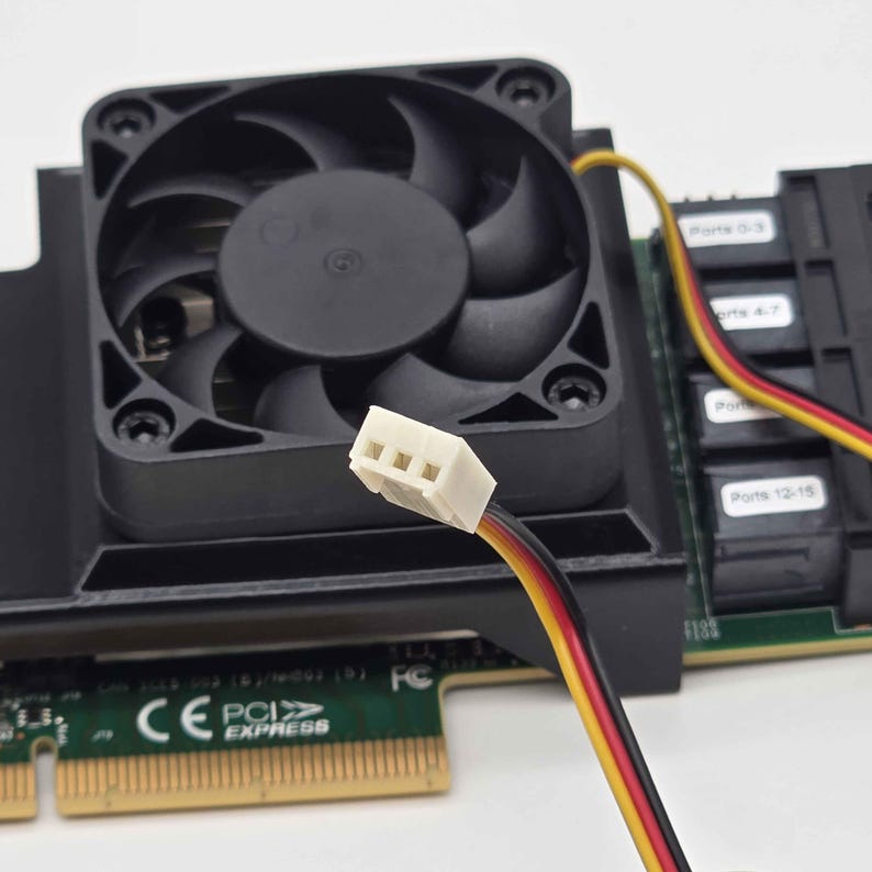 May include: Close-up of a black computer fan with a white connector and multi-colored wires. The fan is mounted on a green circuit board with the text "PCI EXPRESS". The fan blades are visible, and the overall design is for computer hardware.
