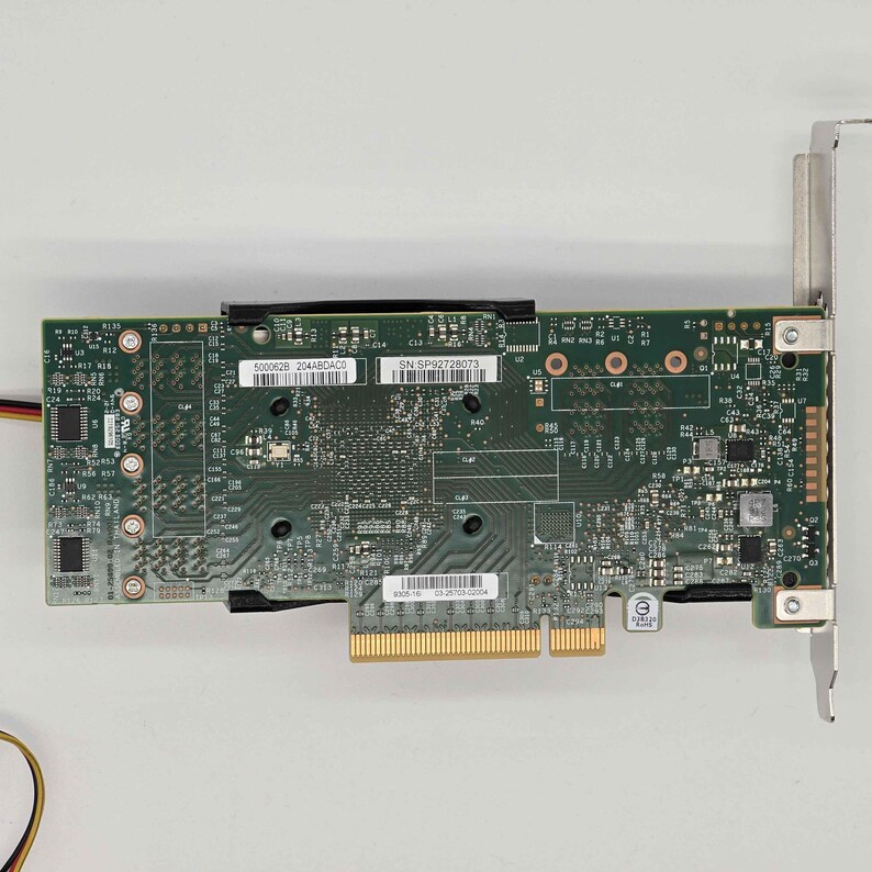 May include: A green circuit board with various electronic components, including chips, connectors, and small circular elements. The board has a gold-colored connector at the bottom and a metal bracket on the right side. The text "500062B 204ABDACO" and "SN: SP92728073" are visible.