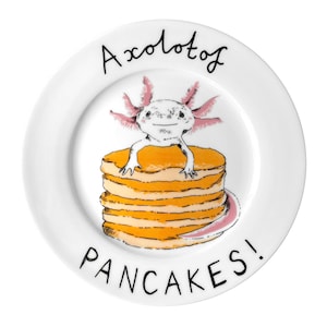 May include: White ceramic plate with a whimsical illustration of an axolotl sitting atop a stack of pancakes. The plate features the words "Axolotl" and "PANCAKES!" in black script, with the axolotl in pink and the pancakes in shades of orange.