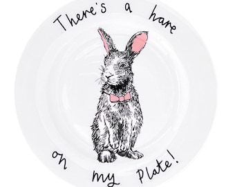 May include: White ceramic plate with a black and white illustration of a rabbit wearing a pink bow tie. The plate has the text "There's a hare on my plate!" written on it.