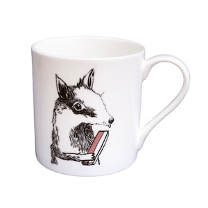 May include: White ceramic mug featuring a black and white illustration of a badger eating a pink and white candy bar.