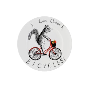 May include: A white ceramic plate with a black and white illustration of a squirrel riding a red bicycle with a basket full of nuts. The text "I Love Cheese & Bicycles!" is written around the squirrel.