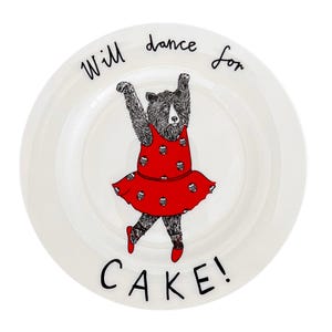 May include: White ceramic plate with a black and white illustration of a bear wearing a red dress with white polka dots. The bear is dancing with its arms raised. The text "Will dance for CAKE!" is written around the bear.