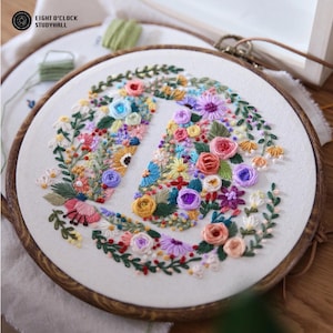 Peut inclure: Un tambour à broder circulaire en bois contenant un tissu blanc avec un motif floral cousu à la main. La broderie présente une variété de fleurs colorées, dont des roses, des marguerites et de la verdure, disposées en cercle. Le texte indique EIGHT O'CLOCK STUDYHALL.