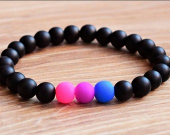 Puede incluir: Un brazalete de cuentas negras con tres cuentas de acento en rosa, morado y azul.