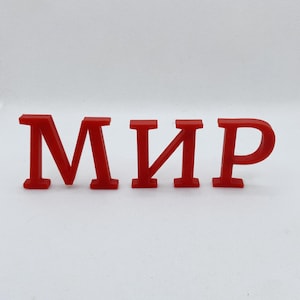 May include: A set of three red, three-dimensional letters forming the Cyrillic word "МИР". Each letter features a bold, serif-style font with a smooth, matte finish, standing upright against a plain, light-colored background.