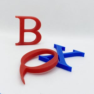 May include: Red letter "B" and red letter "O" with a blue letter "X" on a white background. The letters are 3D printed and have a smooth finish. The letters are in a serif font.