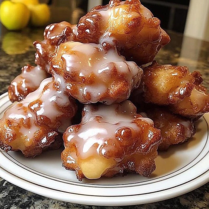 May include: A plate of apple fritters, deep-fried dough with a sweet glaze, piled high on a white plate with a gold rim.
