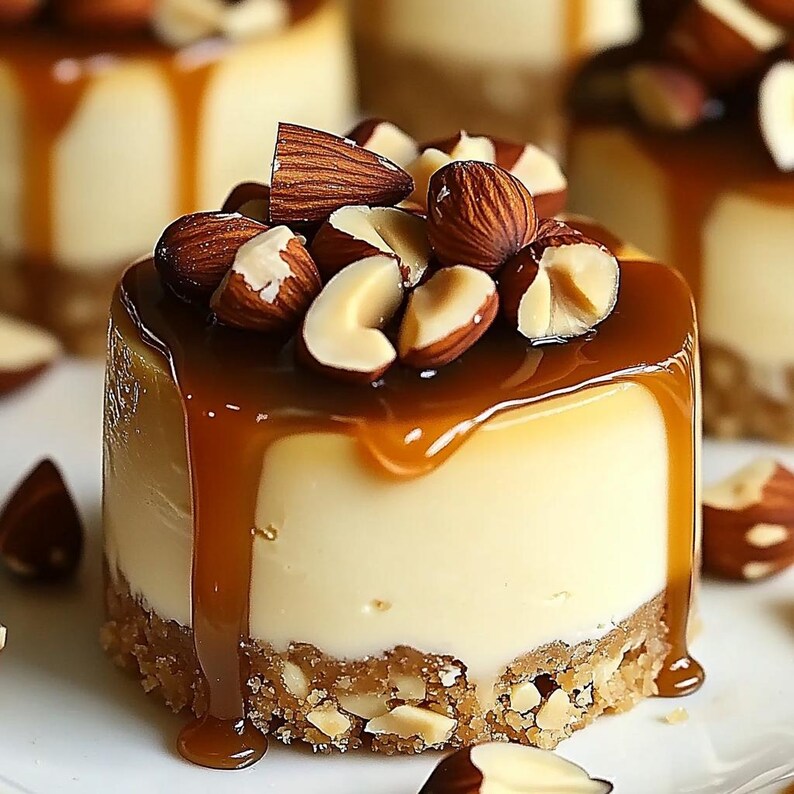 May include: A small cheesecake topped with caramel sauce and chopped almonds. The cheesecake is on a white plate.
