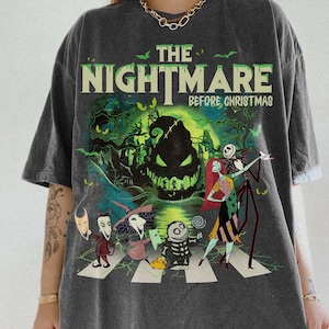 May include: Dark gray t-shirt featuring a graphic from "The Nightmare Before Christmas." The design includes characters crossing a street, with the film's title in green and white. The shirt has a vintage look and the Comfort Colors Pepper logo.